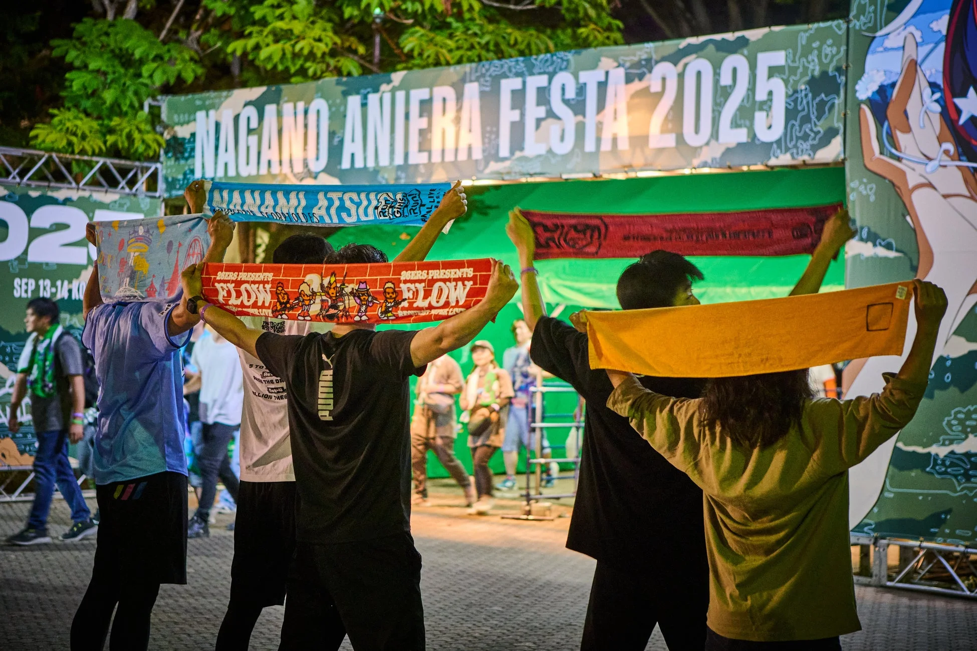 夜の野外イベントで、観客がアーティストのタオルを掲げて盛り上がっている様子