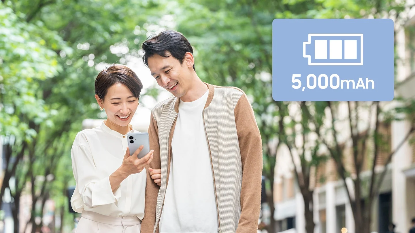 屋外でスマートフォンを見る笑顔のカップル、5,000mAhの表示