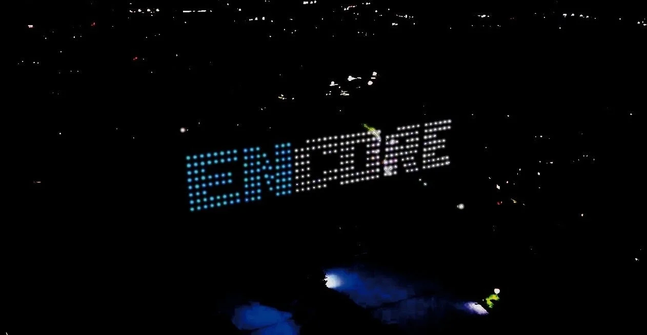 暗い夜空に「ENCORE」という文字が光で大きく描かれている夜景の画像です。遠くには都市の明かりが点々と見え、幻想的な雰囲気を醸し出しています。