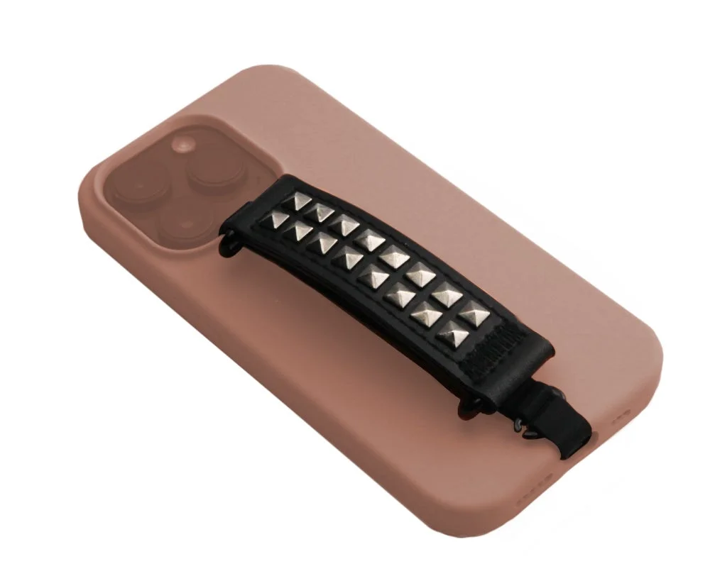 ピンク色のスマートフォンケースに、シルバーのスタッズが施された黒いハンドストラップが取り付けられています。ファッション性と機能性を兼ね備えたスマホアクセサリーです。