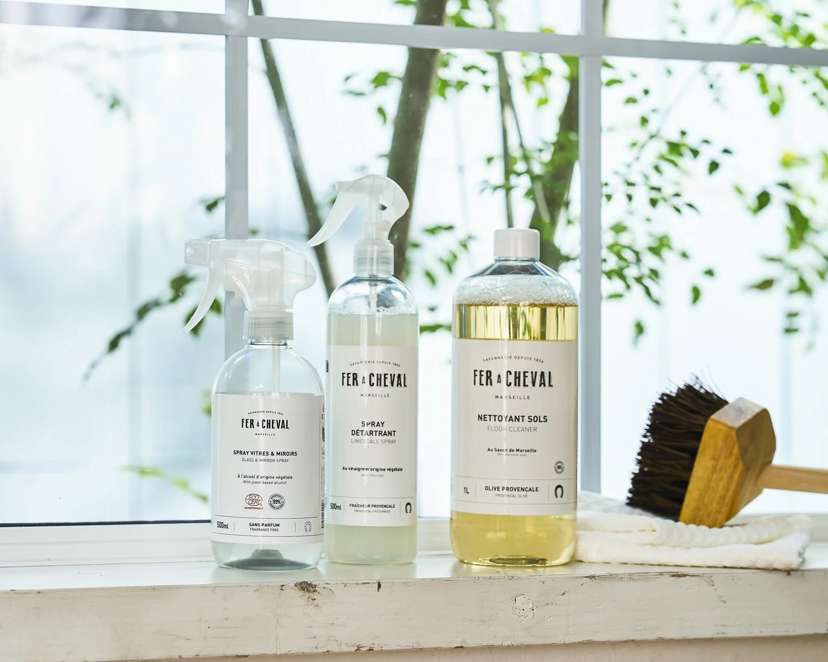 FER A CHEVALのガラス・鏡用スプレー、水垢除去スプレー、床用洗剤の3本と、掃除用ブラシ、白いタオルが窓辺に