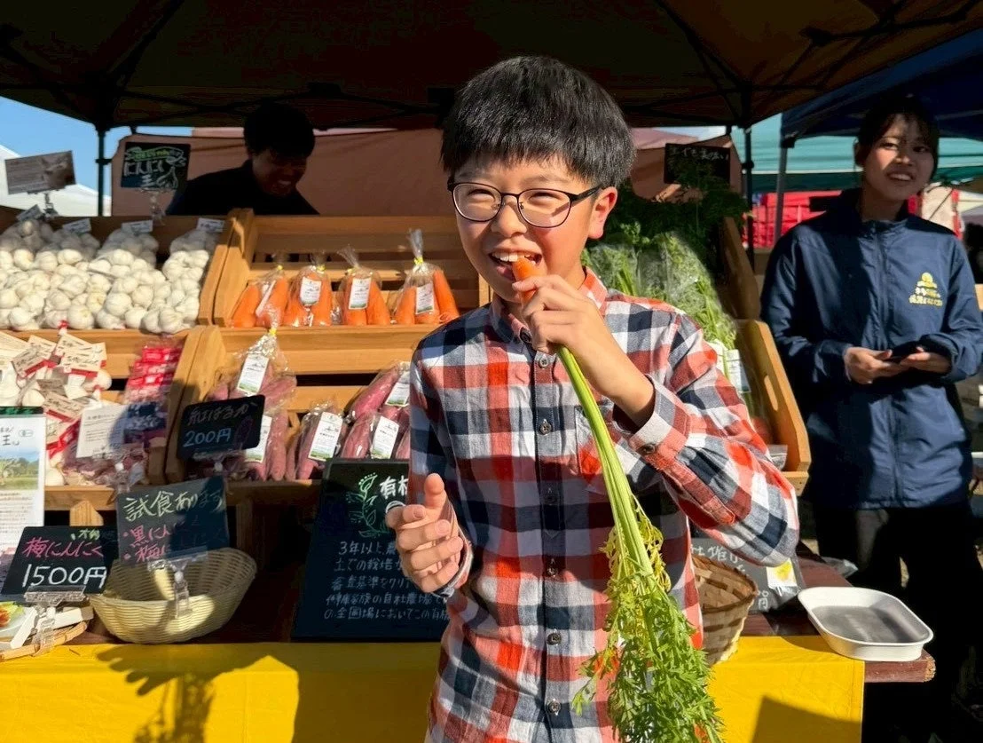 直売所で子供が葉付きのにんじんをかじっている様子