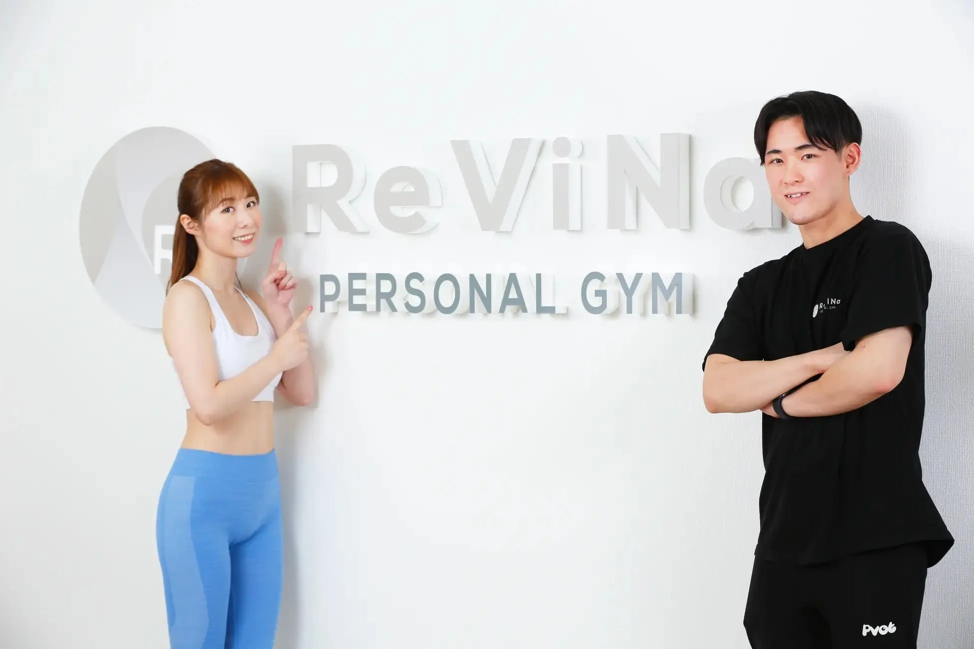ReViNa PERSONAL GYMのロゴが掲げられた白い壁の前で、スポーツウェアを着用した男女が立っている様子