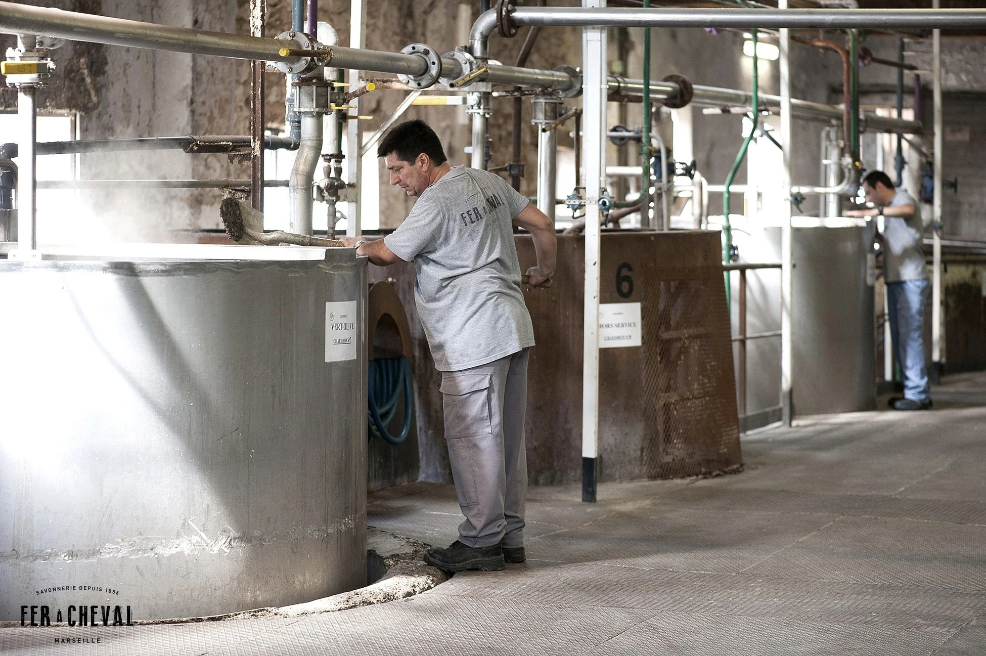 伝統的な石鹸工場で、一人の男性が湯気を上げる大きな釜をかき混ぜている