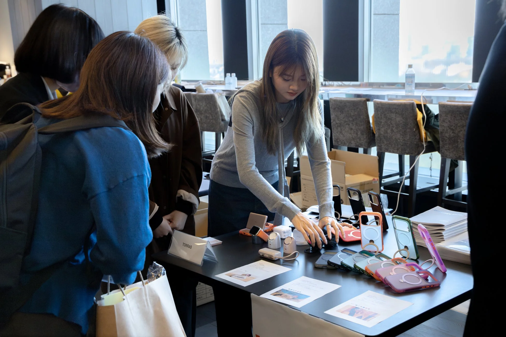 女性たちがスマートフォンケースやガジェットが並ぶブースで商品を見ている様子