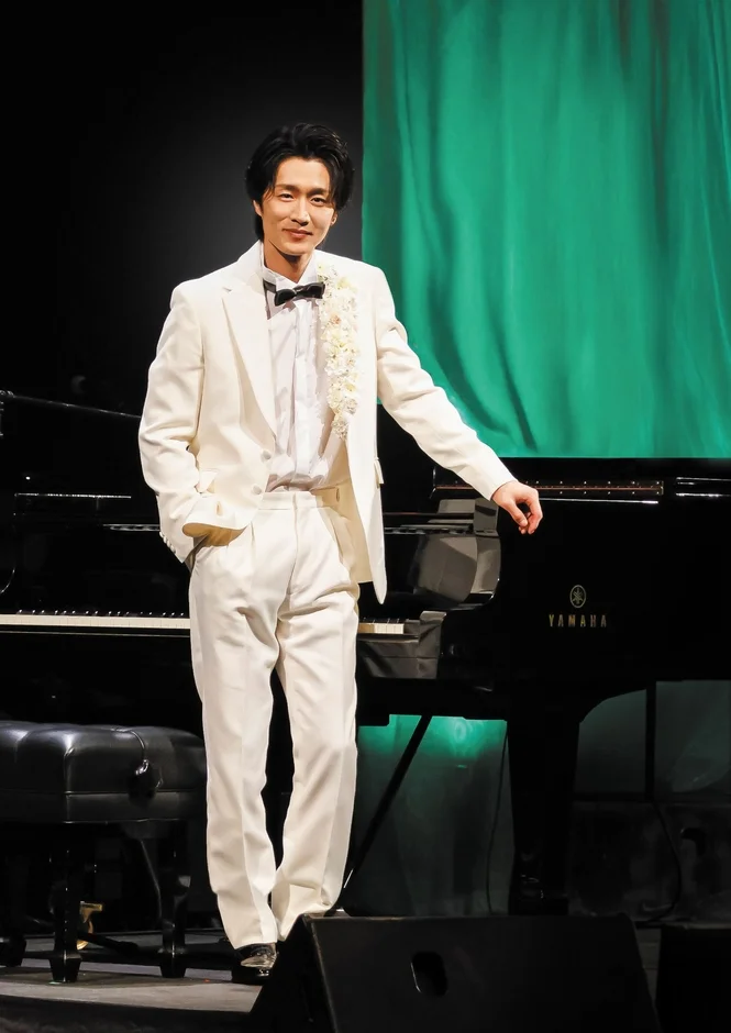 白いタキシードを着てピアノの前に立つ真田ナオキ