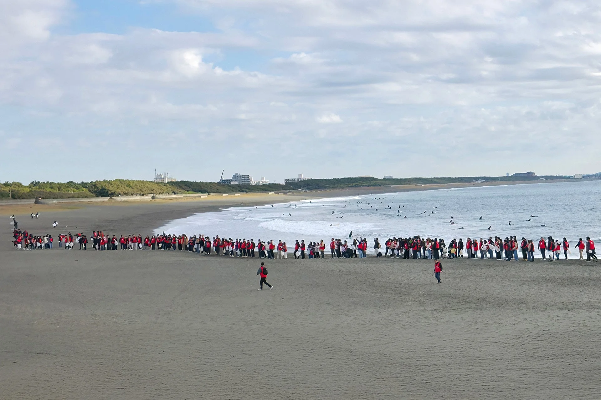 ビーチで整列する参加者と沖合のサーファー