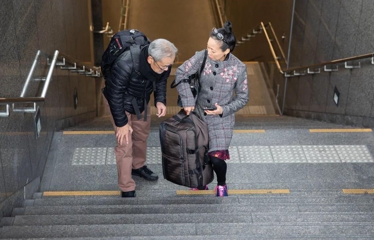 階段で重そうな荷物を持つ高齢の夫婦