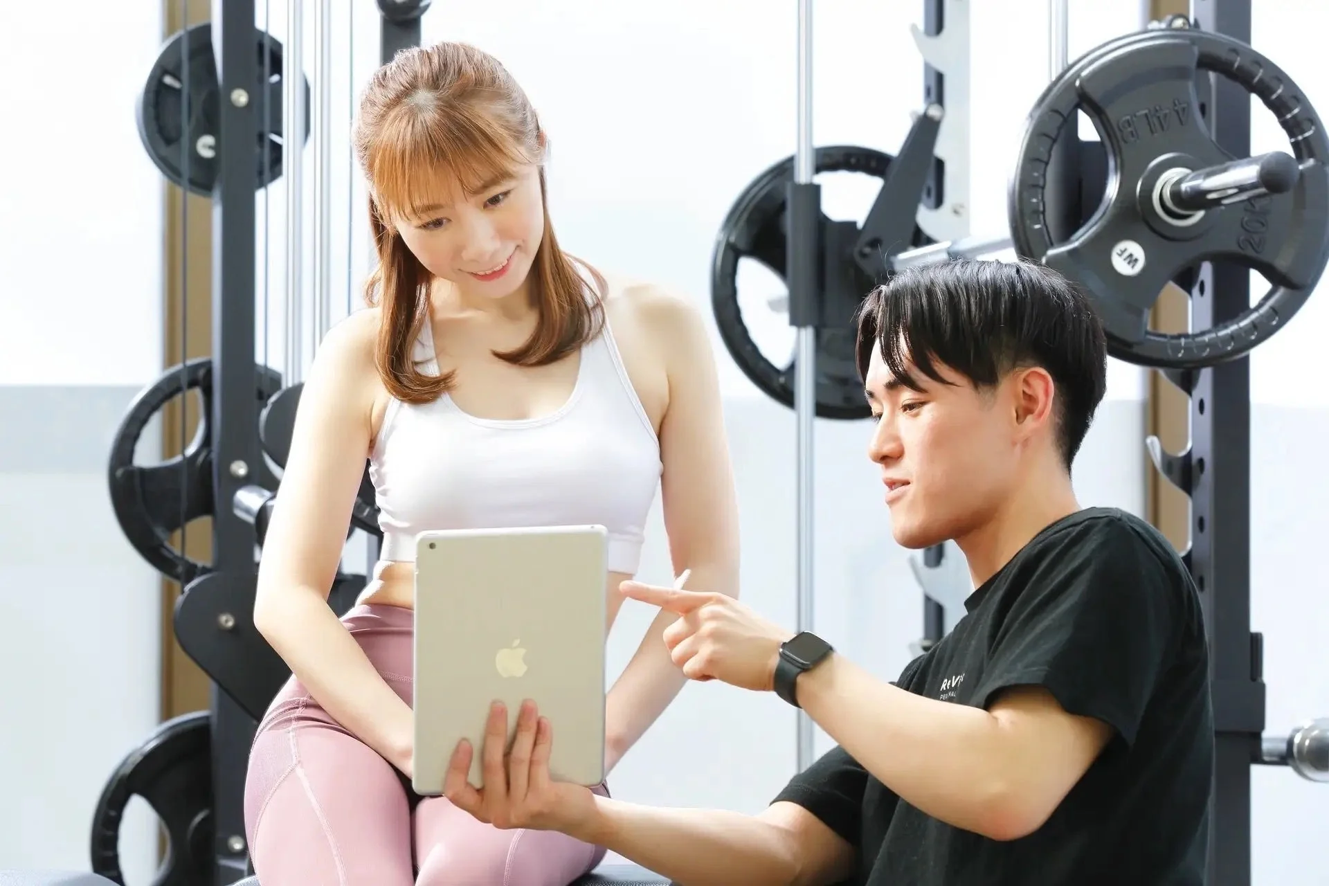 ジムでトレーナーが女性にタブレットでトレーニングプランなどを説明している様子