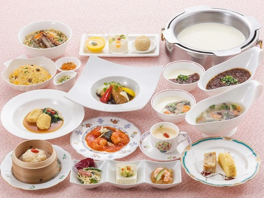 ピンクのテーブルクロスの上に、炒飯、麺、海老チリ、点心、スープ、デザートなど、多種多様な中華料理が豪華に並べられた食卓の様子。