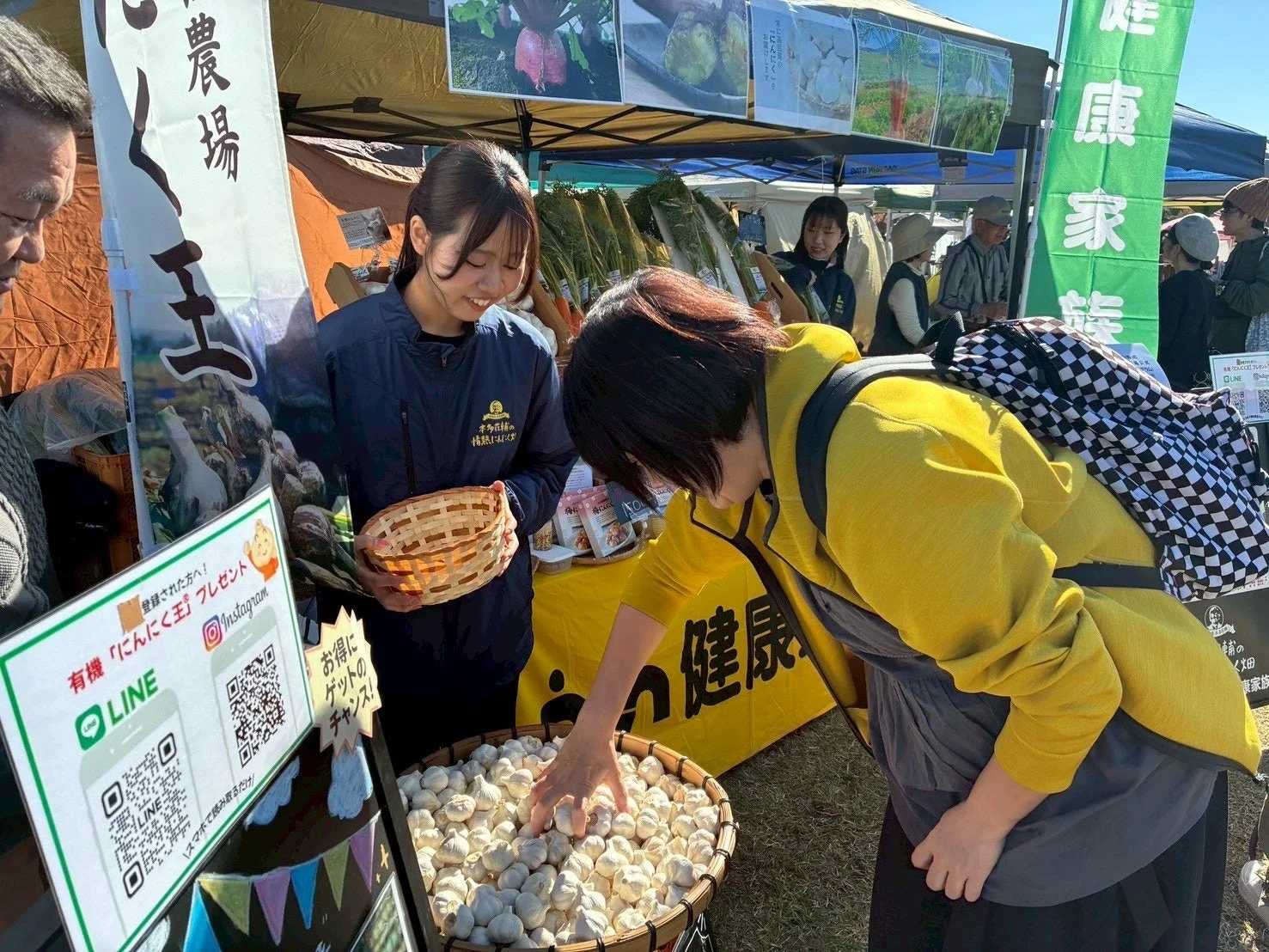 屋外マルシェで客がにんにくを選んでいる様子