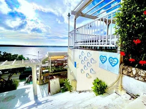 青い空と海が広がる開放的なテラス席がある施設の階段からの眺め。ハート型の装飾と植物が配置されています。