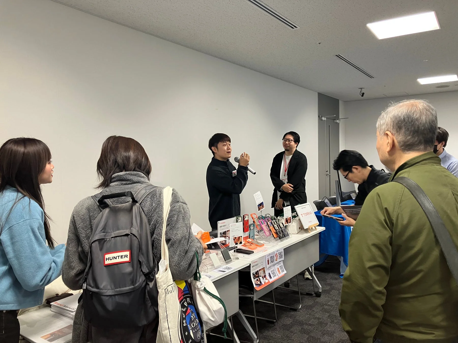 男性がマイクを手に製品を説明している屋内イベントの様子