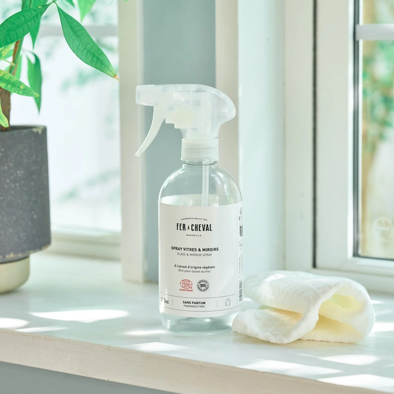 植物由来の窓・鏡用スプレーと白いタオルが窓辺に置かれている