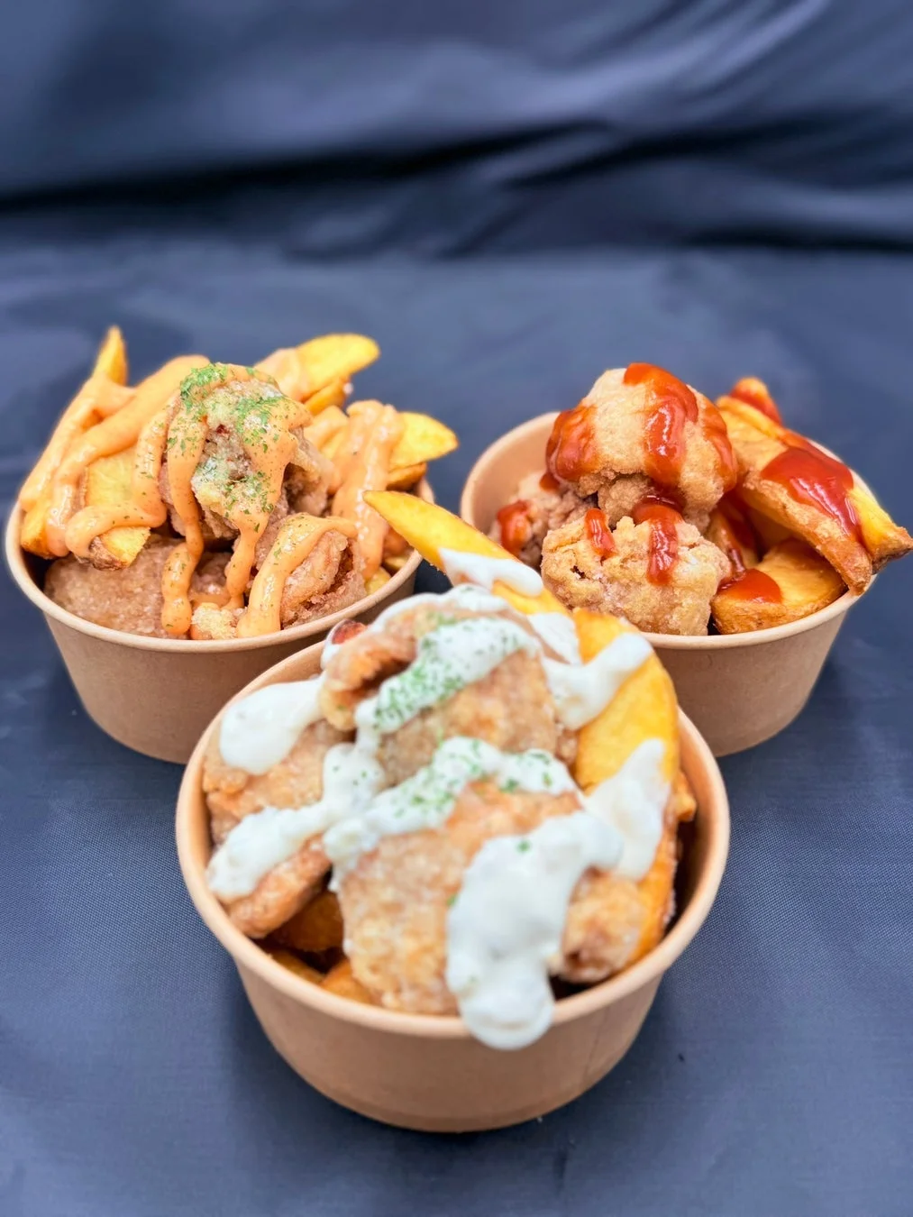 3つの紙カップに入ったフライドチキンとポテトウェッジの盛り合わせです。