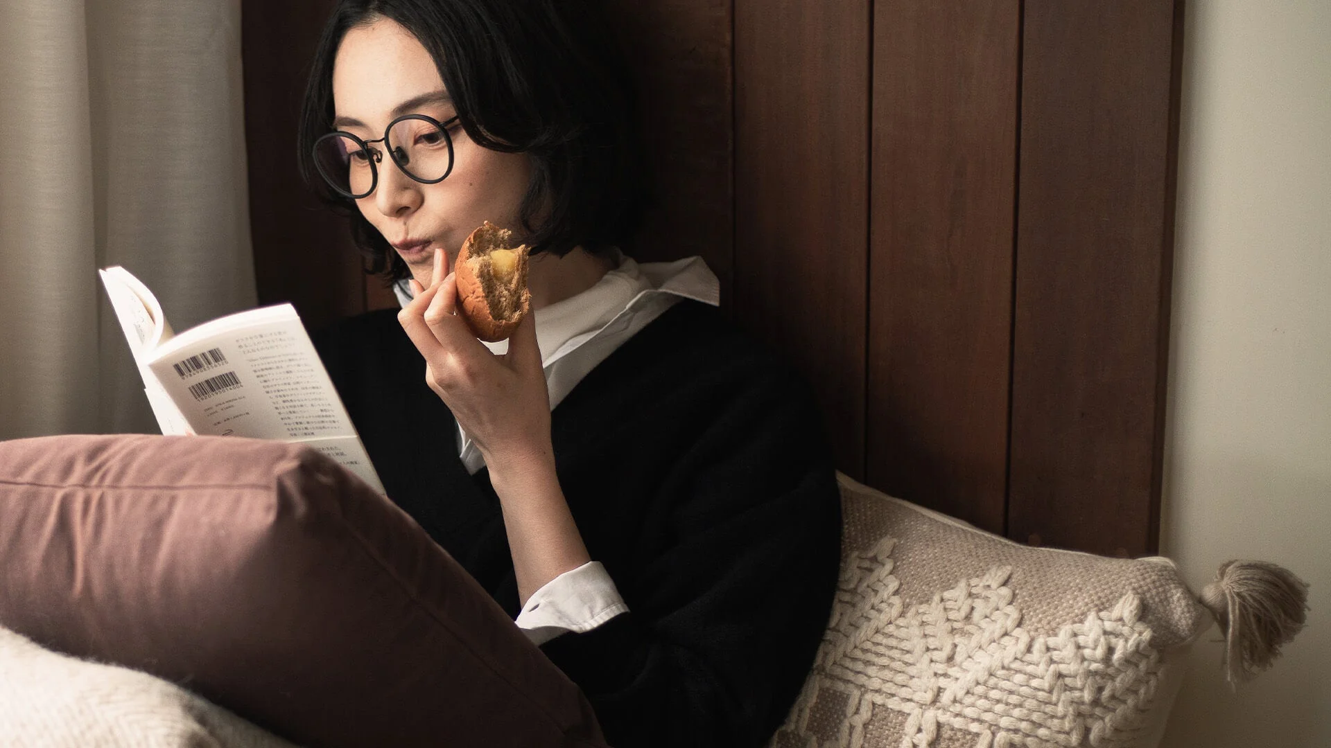 女性が本を読みながらパンを食べている