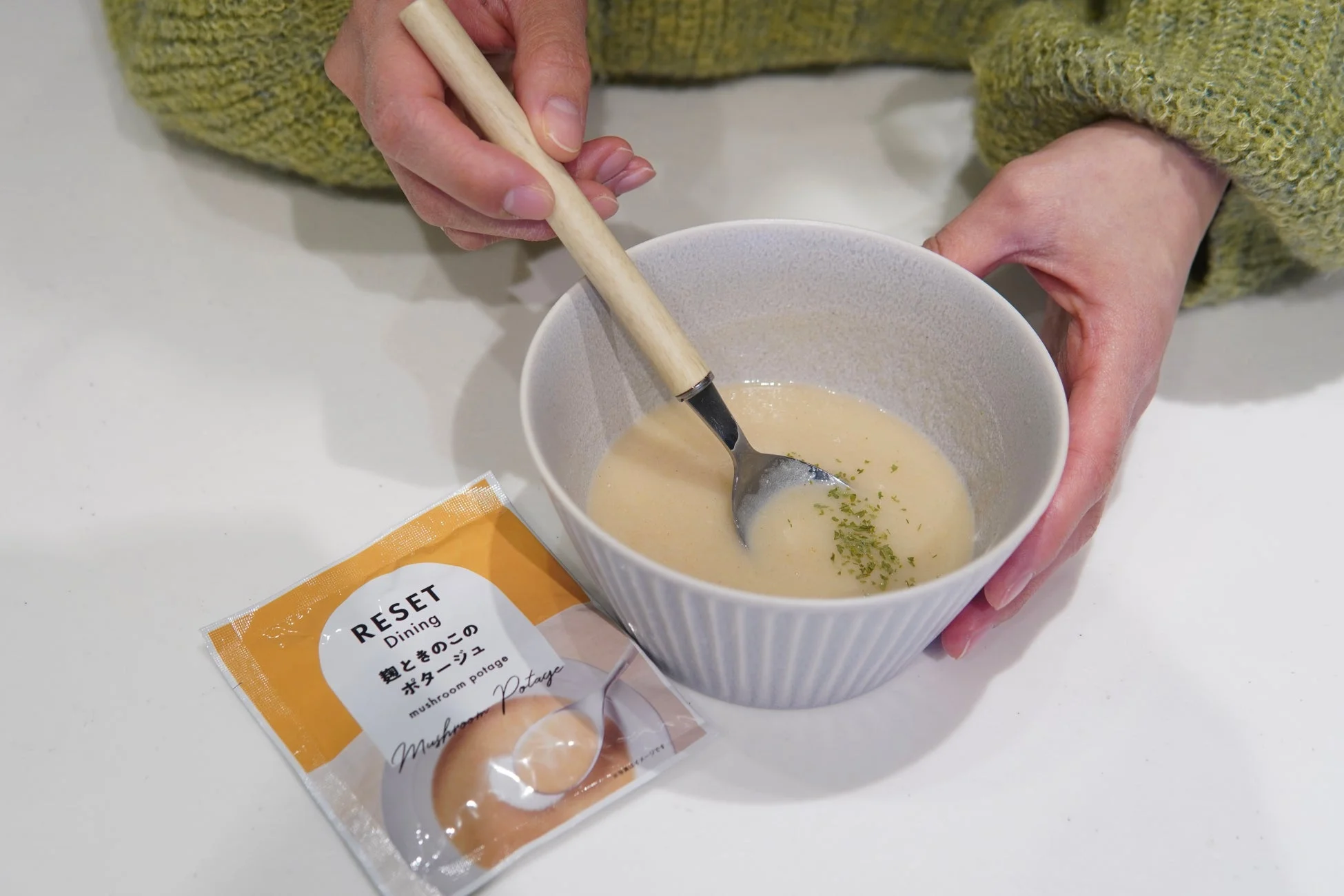 緑色のセーターを着た人物がきのこポタージュを混ぜる手元