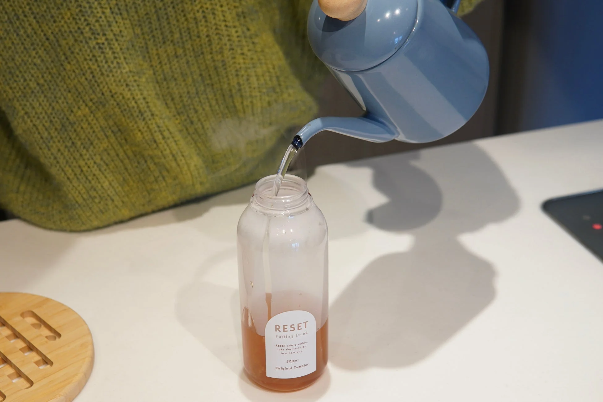 緑色のセーターを着た人がRESET Fasting Drinkのボトルに水を注ぐ様子