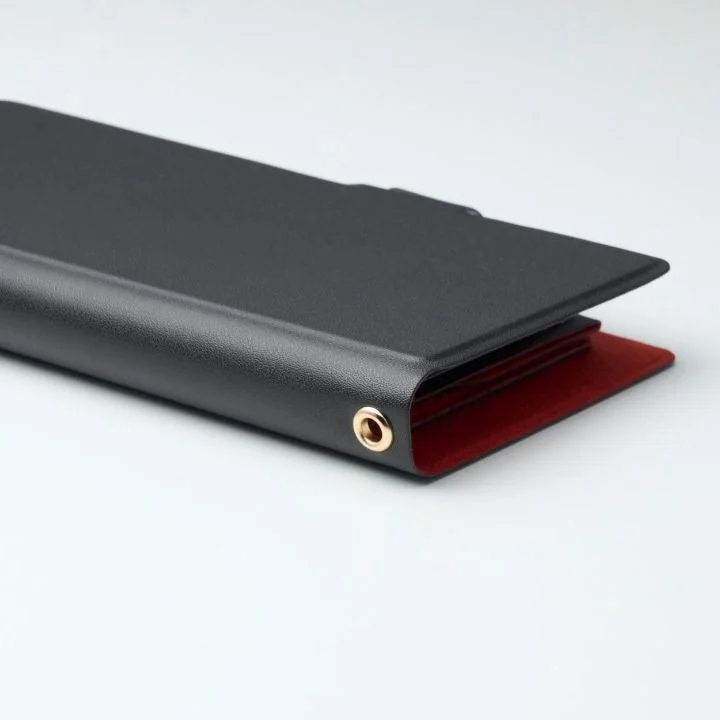 黒いバインダーまたはファイルフォルダが写っており、内側は鮮やかな赤色で、側面に金色のハトメが一つ付いている様子