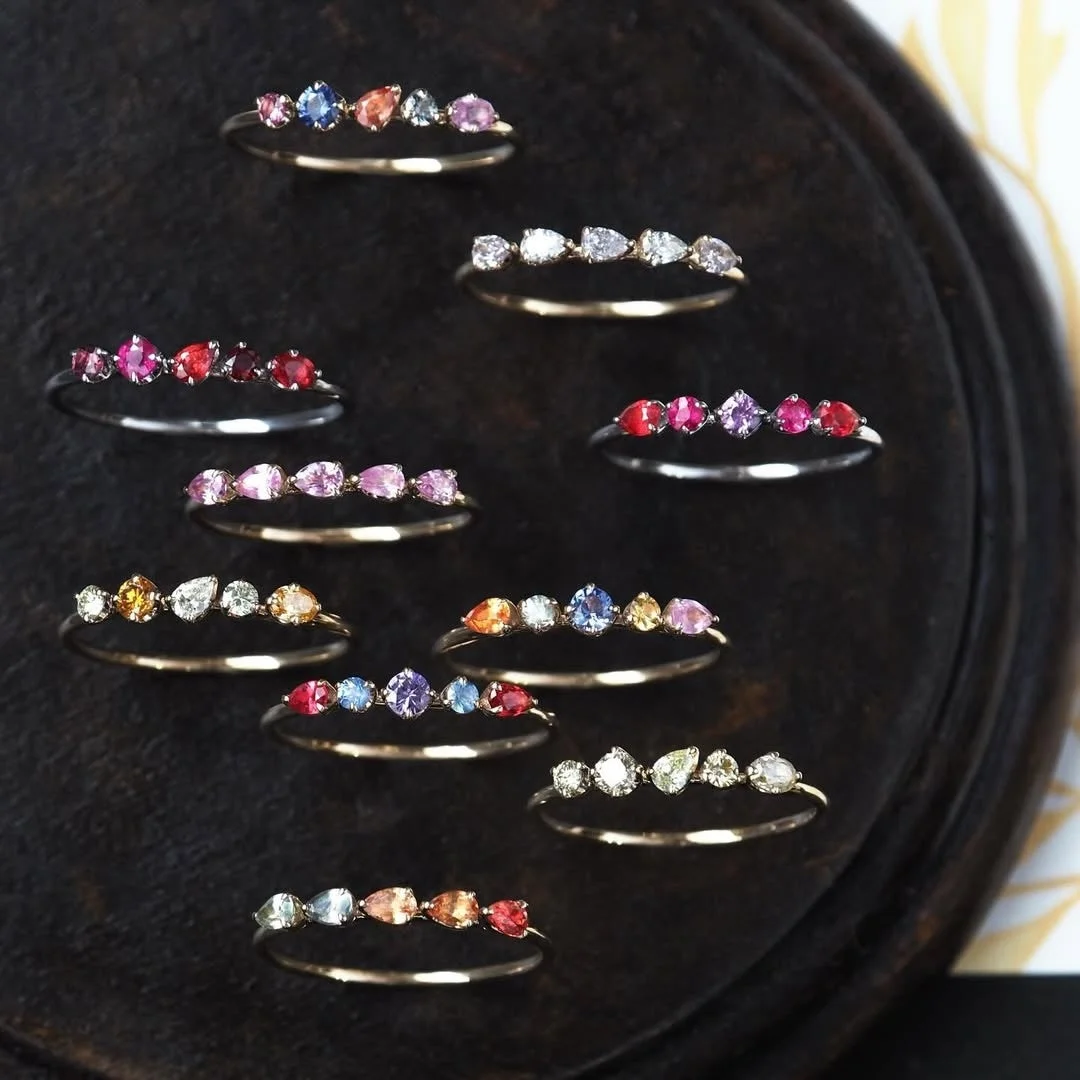 暗い背景の上に、様々な色と形の宝石が散りばめられた複数の指輪が美しく配置されている