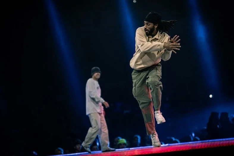 青い照明が当たる暗いステージで、2人の男性ダンサーがパフォーマンスを披露している様子