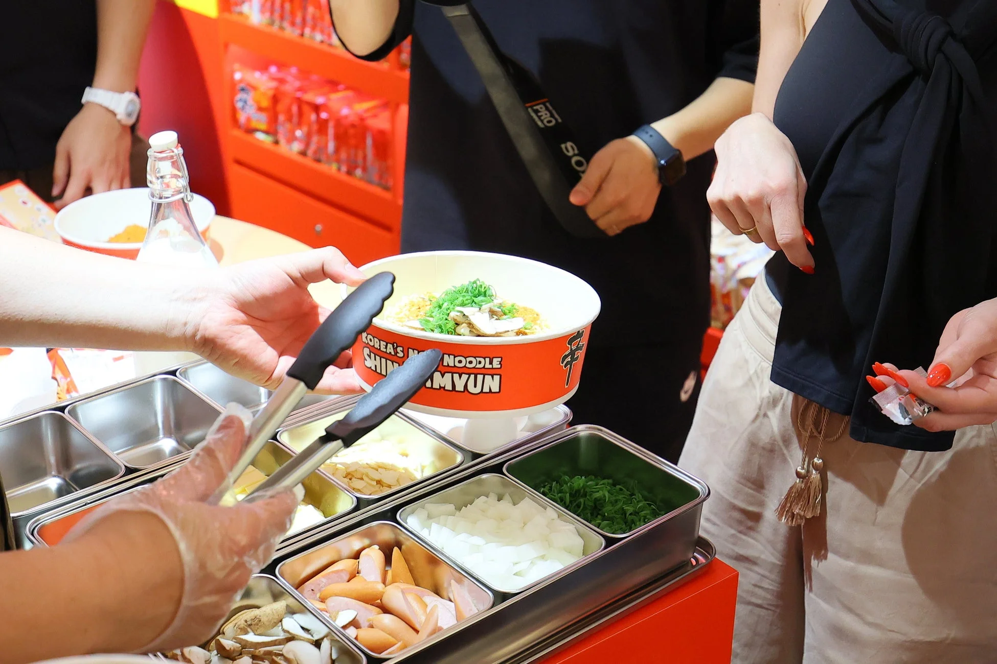 セルフサービスのコーナーで、辛ラーメンのカップ麺に様々なトッピングを加えている様子です。