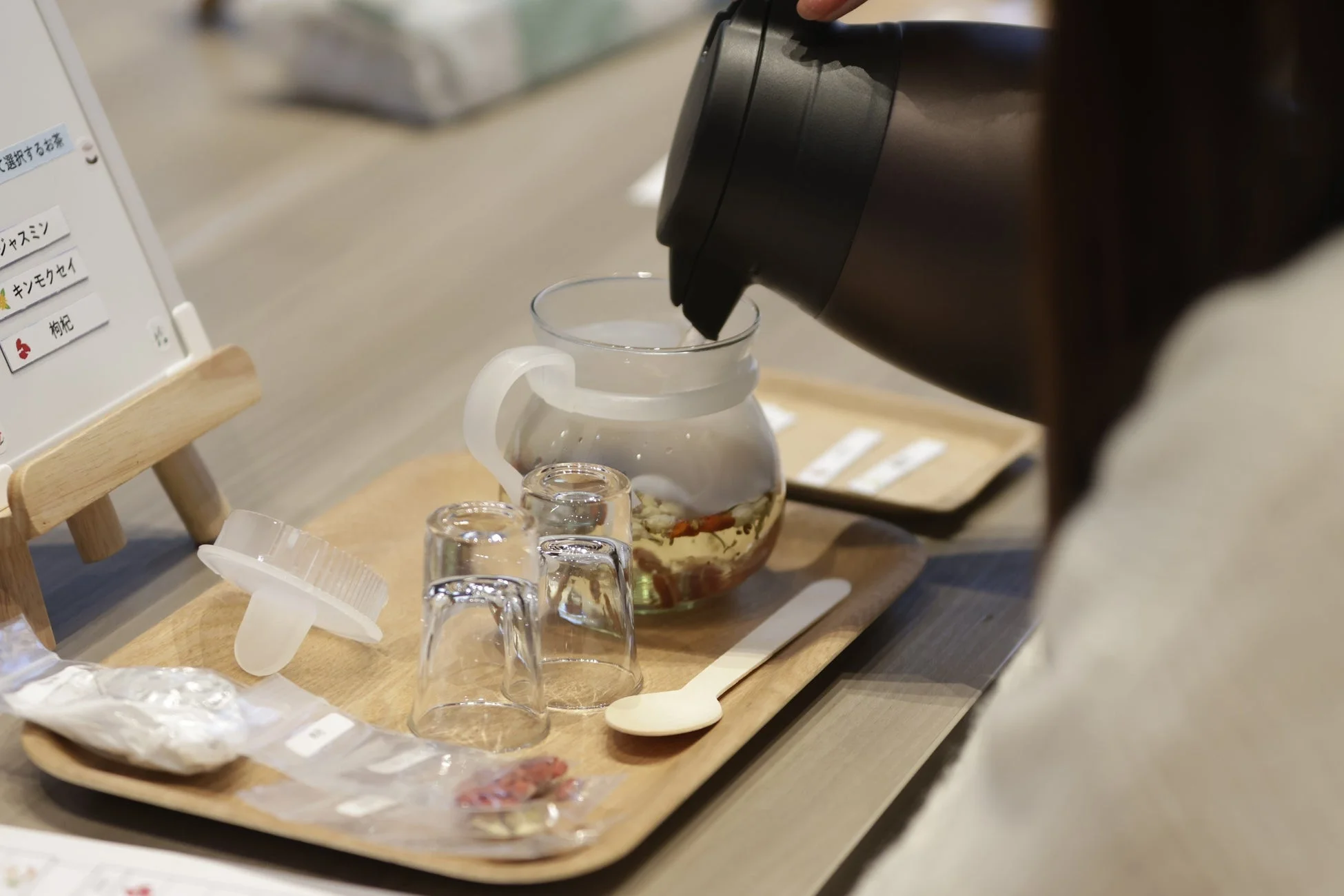 木製トレイに置かれたティーポットに、サーモボトルから温かいお湯を注いでいる様子