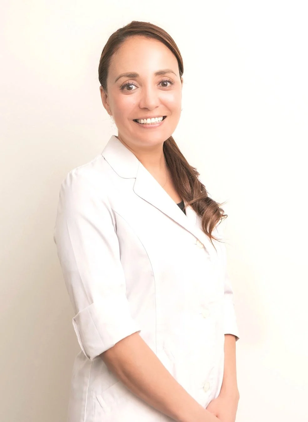 白衣を着て聴診器を首にかけた若い男性医師が、白い背景の前で笑顔で立っているポートレート写真