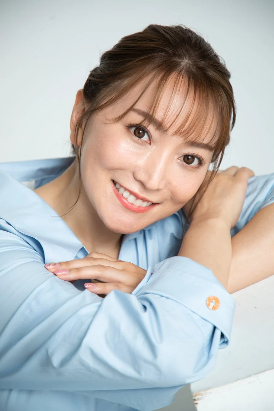 水色のシャツを着た日本人女性がカメラに向かって明るい笑顔を見せています