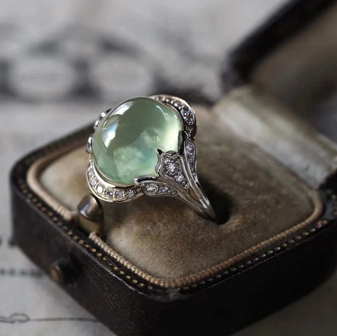 開いたリングボックスに収められた、ライトグリーンのカボションカットの宝石が特徴的なヴィンテージ風リング