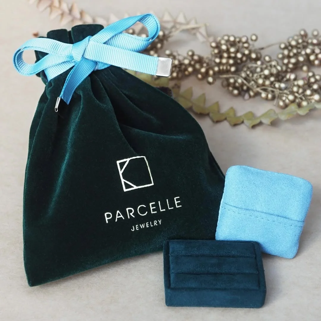 PARCELLE JEWELRYのロゴが入った深緑色のベロア製巾着袋と、水色と深緑の小さなジュエリーボックス