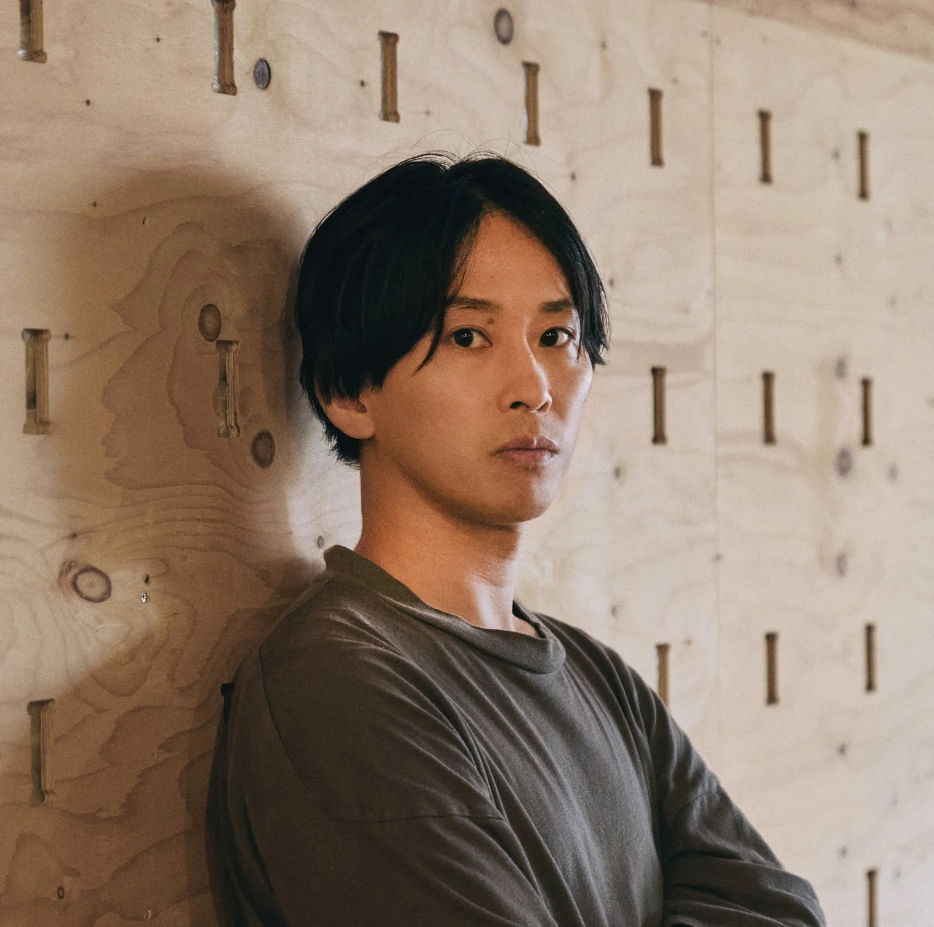 木製の壁にもたれかかりカメラを見つめる男性のポートレート