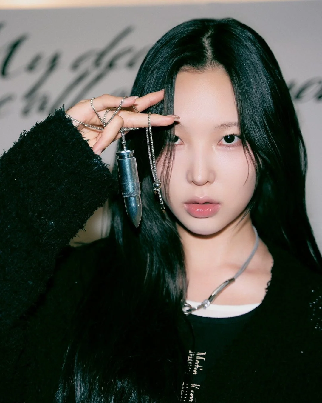 黒いカーディガンを羽織り、銀色の弾丸型ペンダントを見せる女性