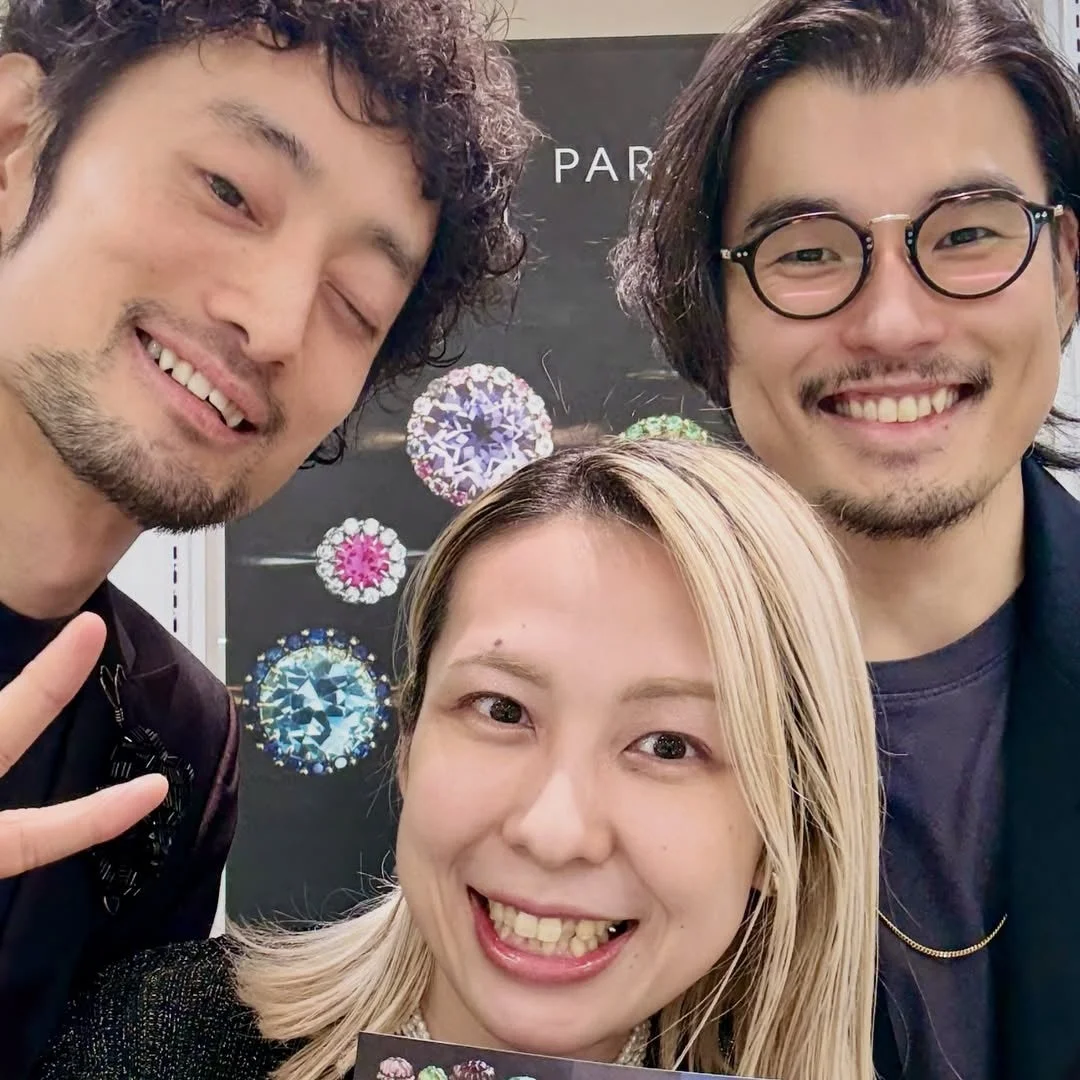 笑顔の男女3人が、カラフルな宝石のディスプレイの前でセルフィーを撮っている様子