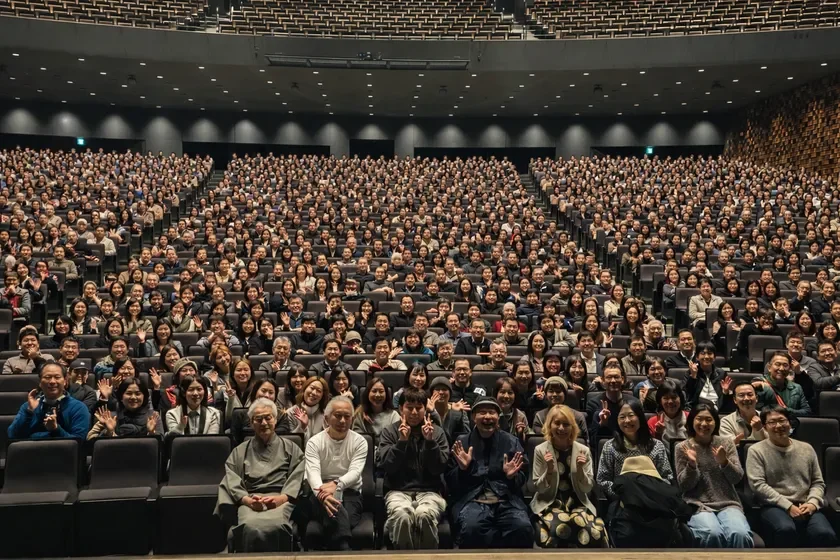満員の観客席で多くの人々が笑顔で手を振っている様子