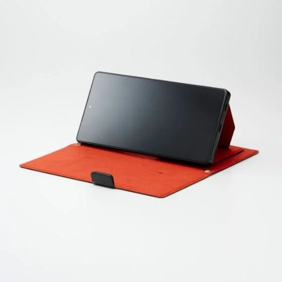 赤い折りたたみ式ケースをスタンドとして使い、横向きに立てられた黒いタブレットまたはスマートフォンが写っている様子
