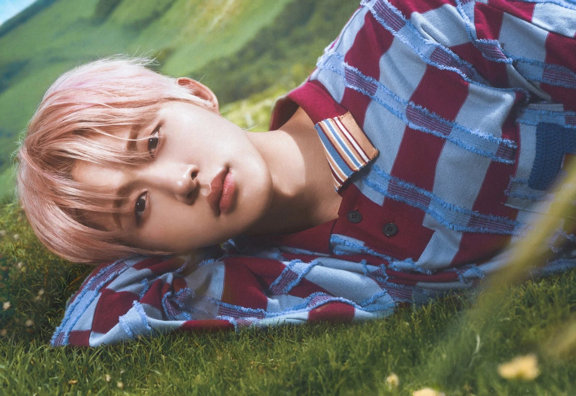 ピンク髪で草の上に横たわるB.I