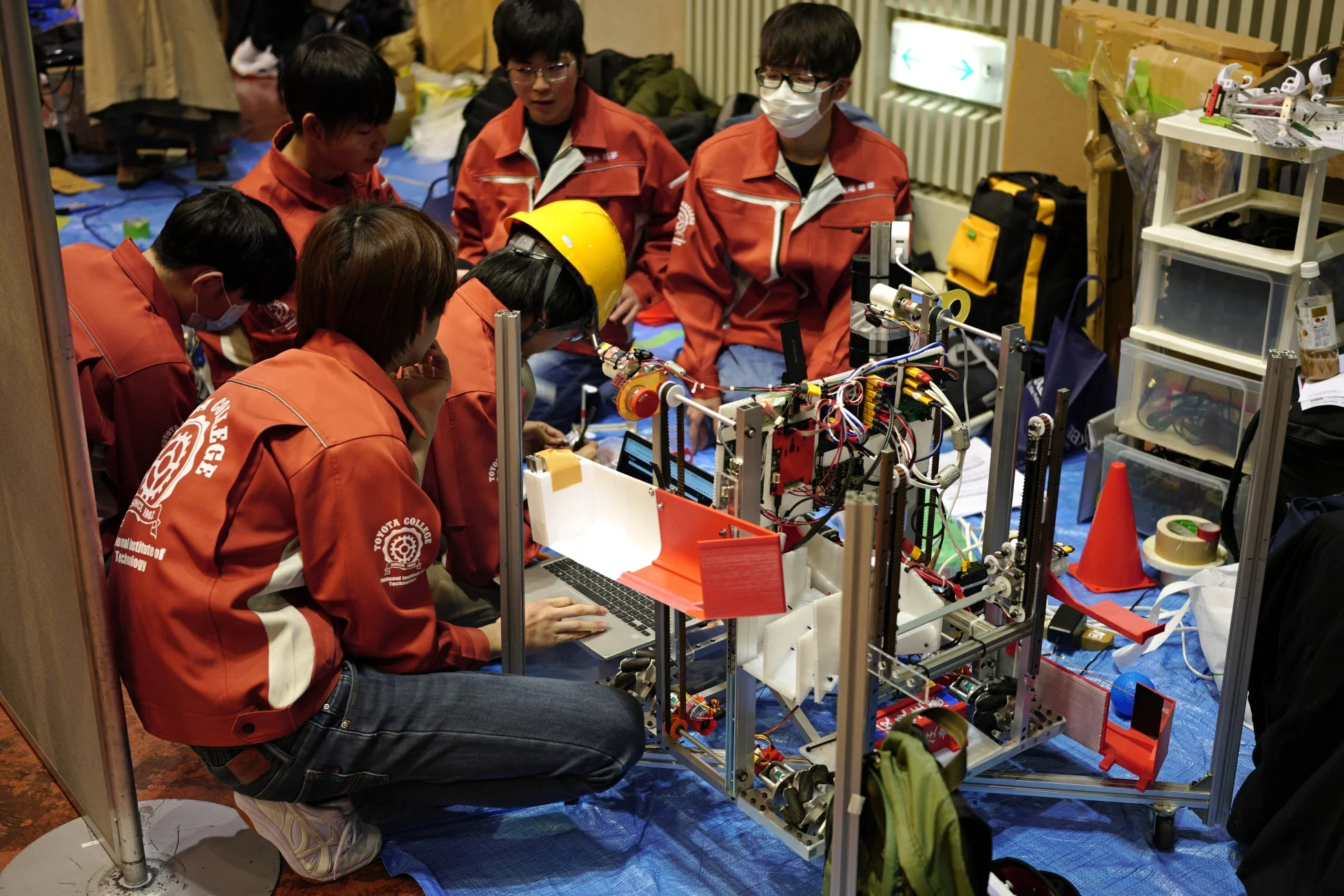 高等専門学校の学生たちがロボットの組み立てや調整作業を行っている様子