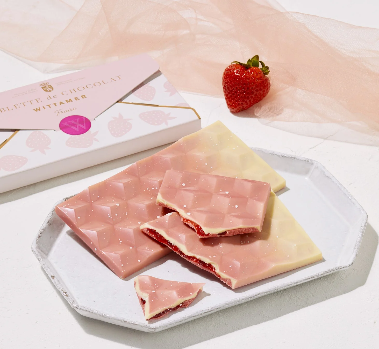 ピンクと白の板チョコレートが白い皿に盛られ、一部は割れていちごのフィリングが見えています