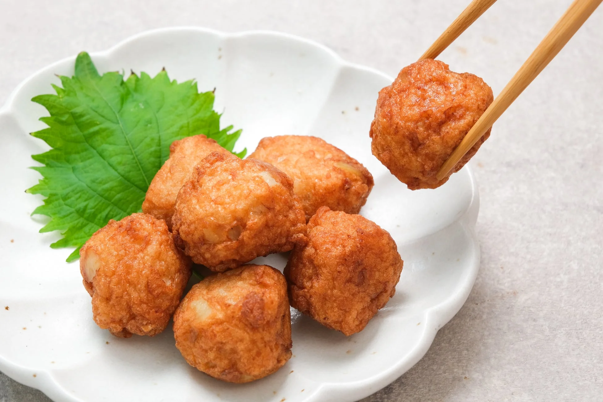 白い皿に盛られた数個の揚げ物（薩摩揚げ）と、添えられた大葉が写っています。箸で一つが持ち上げられており、温かそうな食欲をそそる一品です。