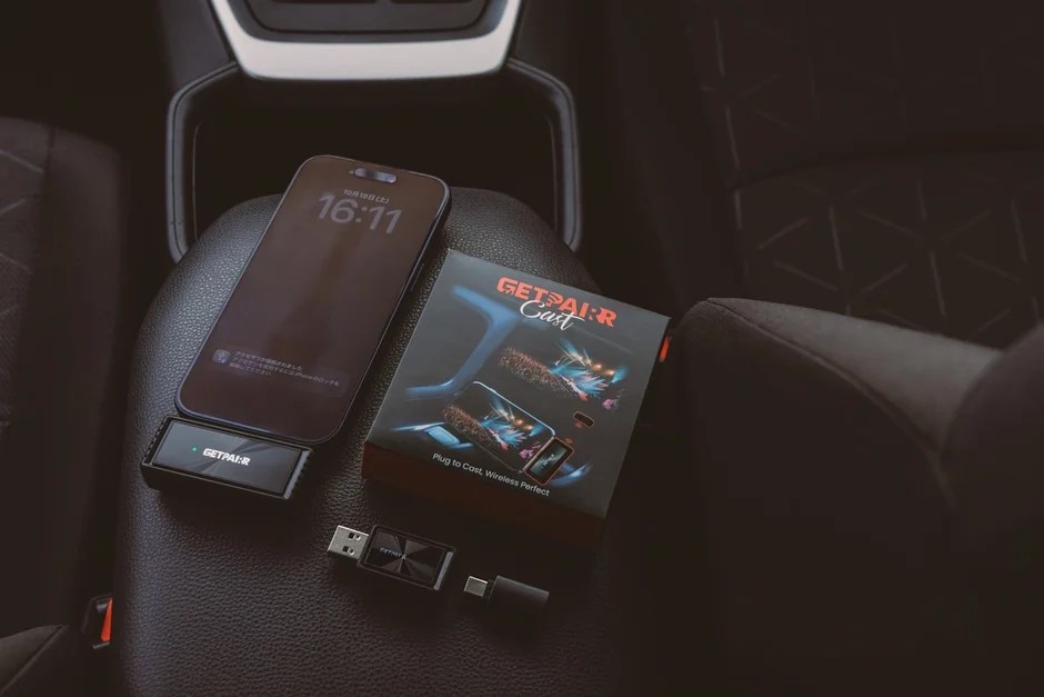 車内の座席に置かれたiPhoneと、ワイヤレス接続デバイス「GETPAIR:R Cast」のパッケージおよび関連アダプターが写っています。iPhoneの画面には「アクセサリが検出されました」というメッセージが表示されています。
