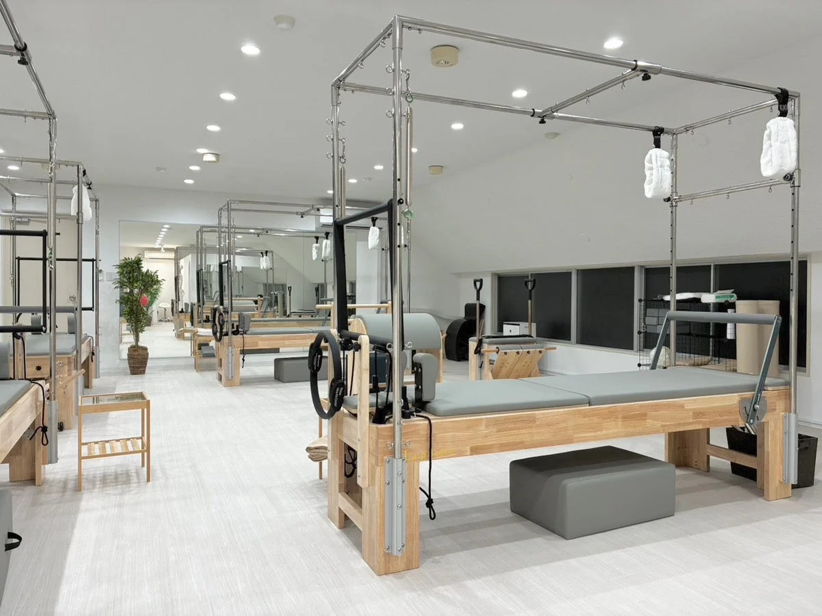 明るく清潔感のあるピラティススタジオで、複数のリフォーマーマシン