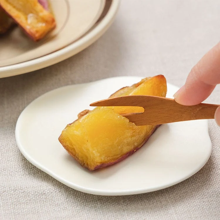 焼かれたさつまいもを白い皿に乗せ、木製のフォークでつまんでいる様子です。温かみのある色合いで、美味しそうな秋の味覚が表現されています。
