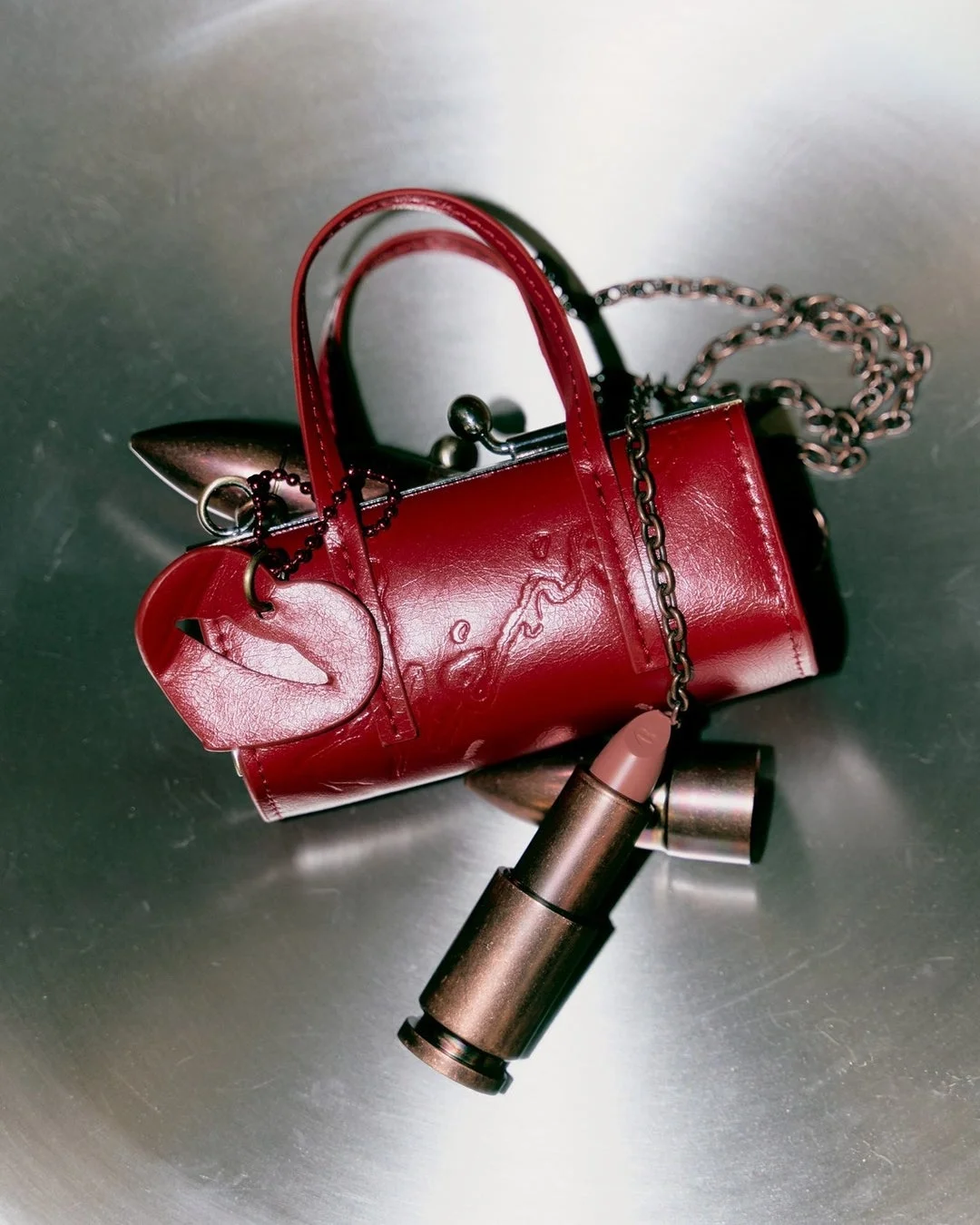 チェーンストラップ付きの赤いミニハンドバッグと弾丸型のヌードカラーの口紅