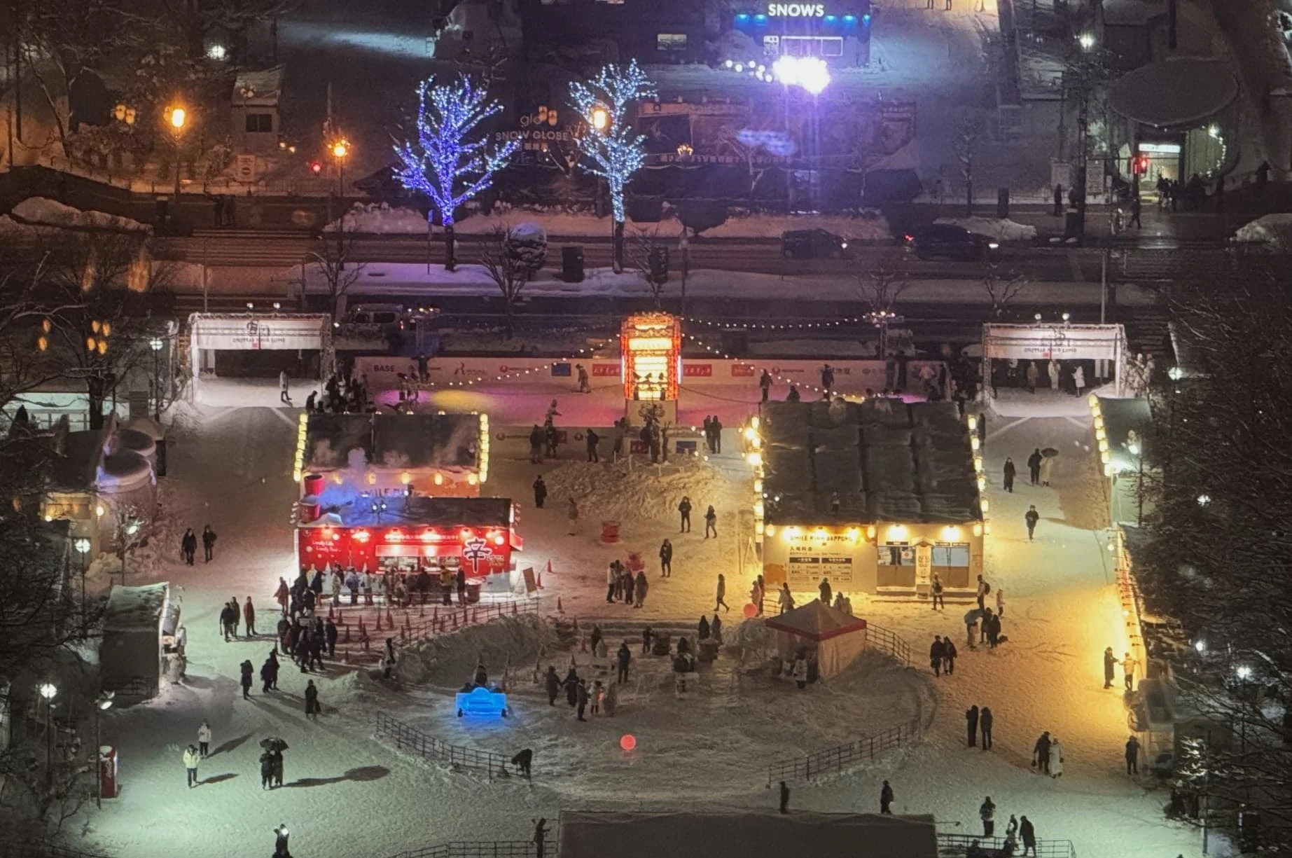 雪降る冬の夜、多くの人々で賑わう屋外イベント会場の俯瞰写真。