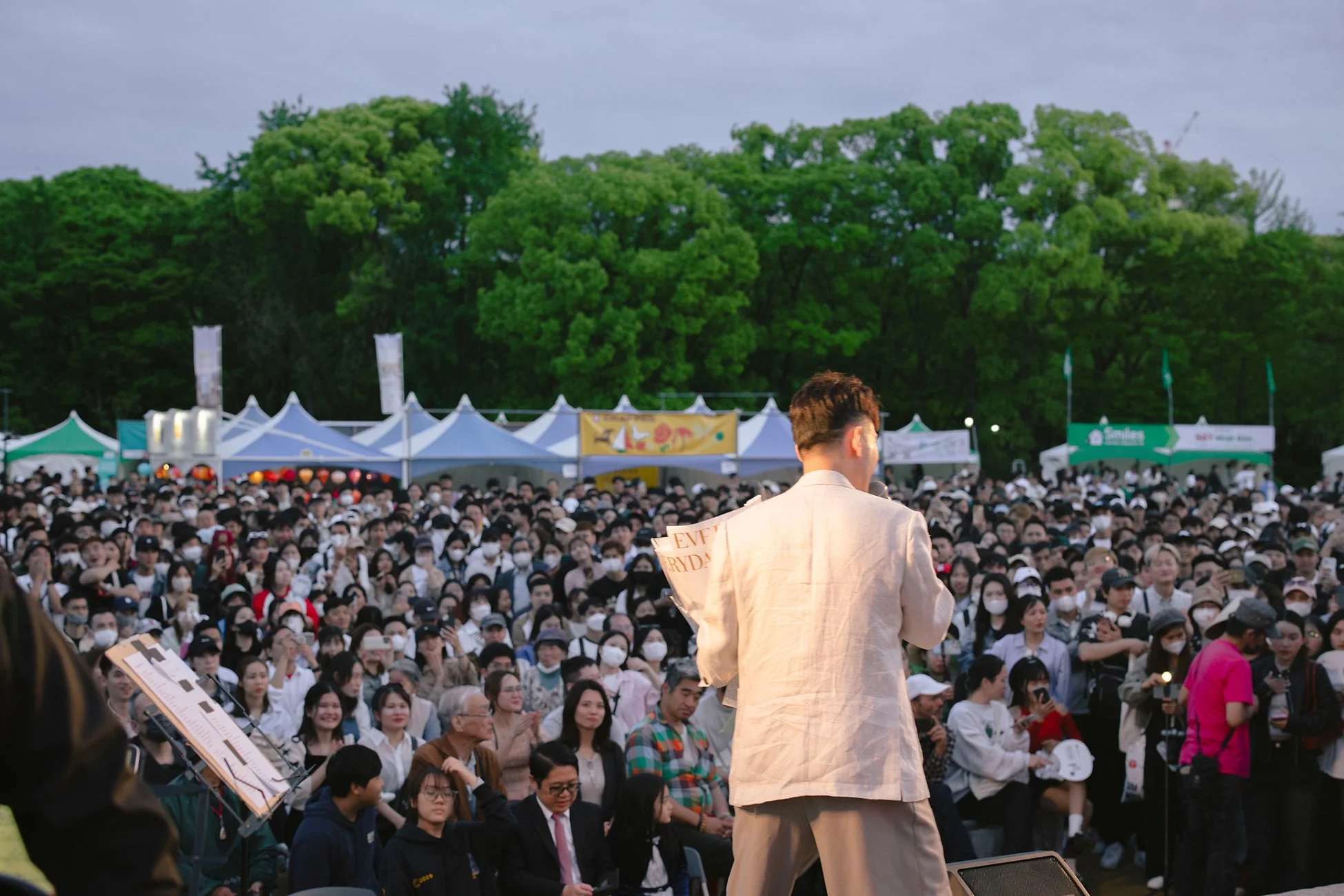 夕暮れの屋外イベントでステージ上のスピーカーが大勢の観客に向けて話している様子