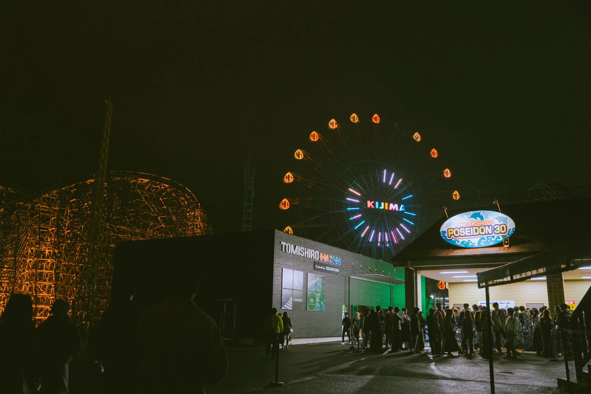 夜の観覧車とアトラクションを楽しむ人々