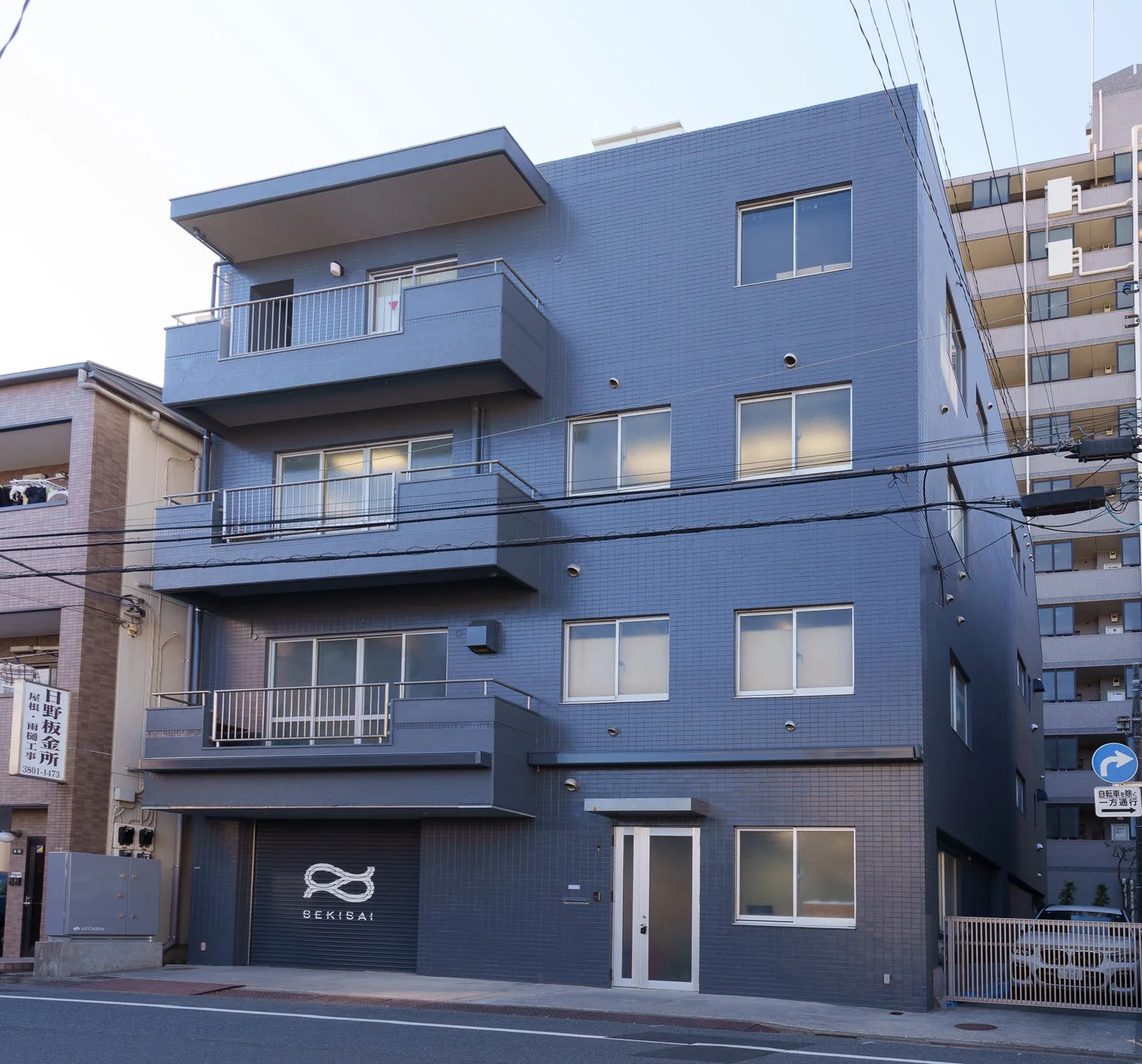 都市部に建つ青みがかったグレーのモダンなビルディング。1階には「SEKISAI」の看板