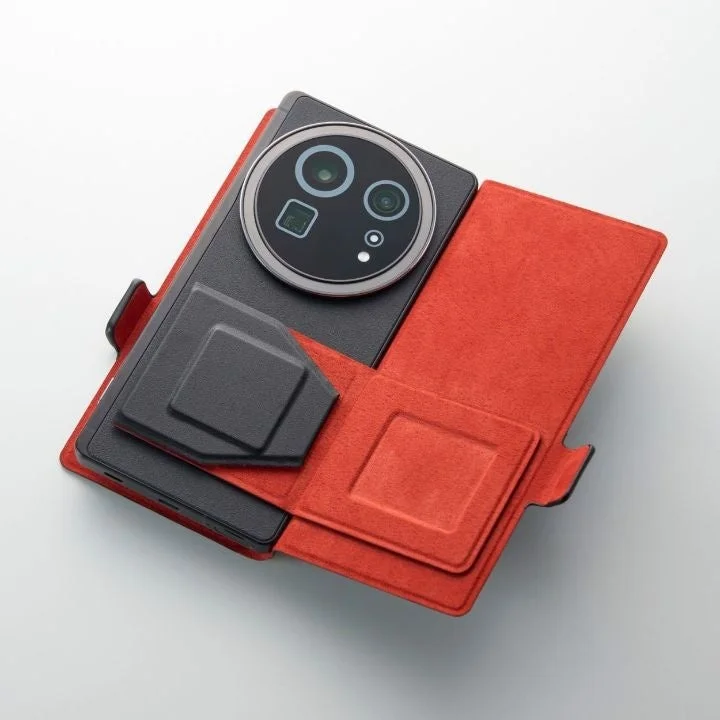 大きな円形カメラモジュールを持つ黒いスマートフォンが、開いた状態の赤いフリップ型ケースに収められている様子