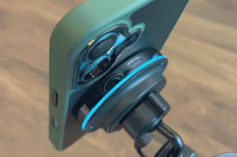 緑色のスマホケースに入ったスマートフォンの背面に、青いLEDが光るマグネット式アクセサリーが取り付けられています